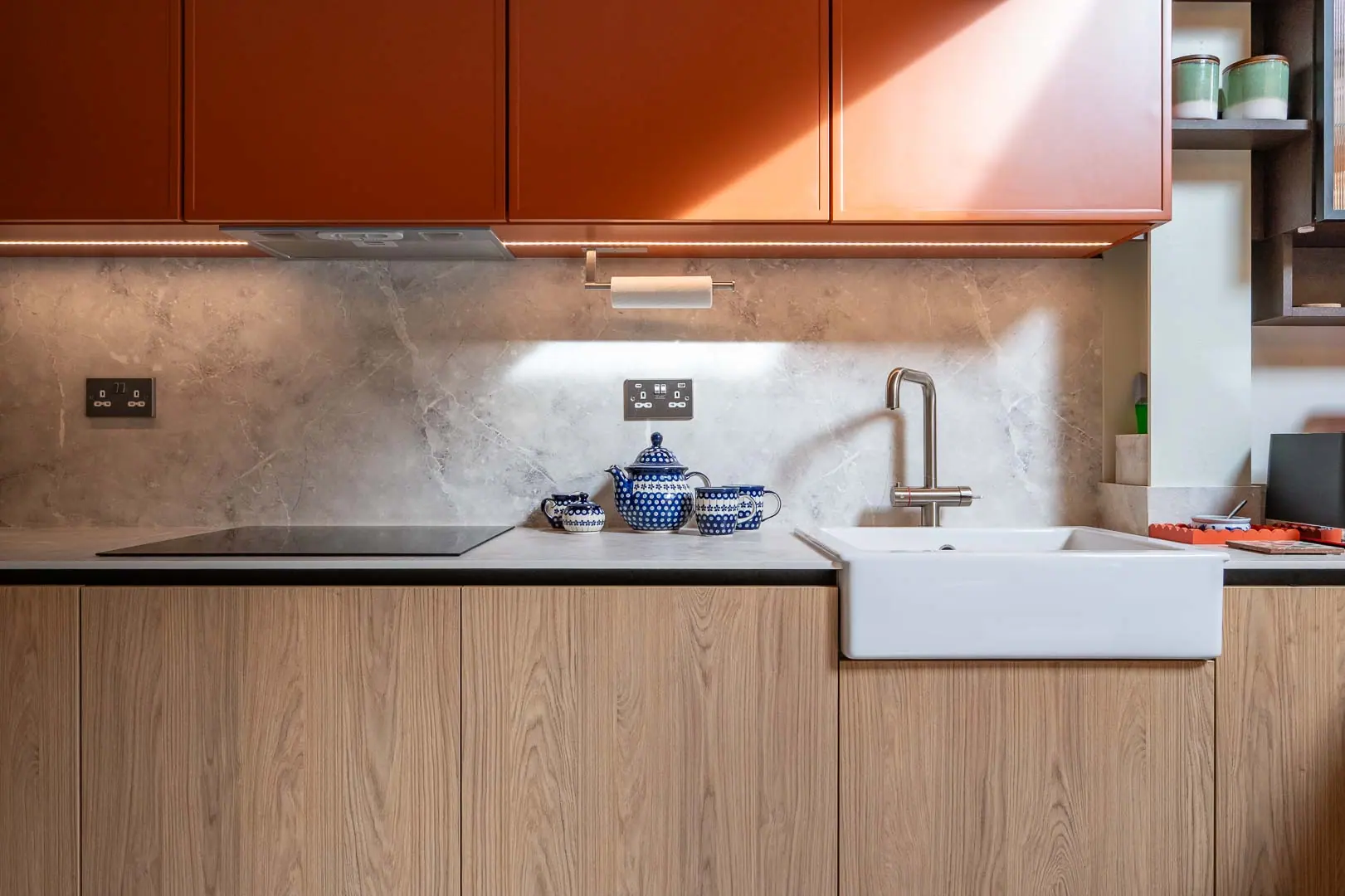 Stone splashback, induction hob and a deep sink beneath lit wall units.
