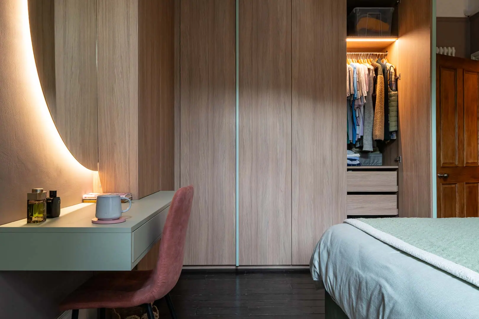Fitted wardrobes and a dressing table under a curved, backlit mirror.